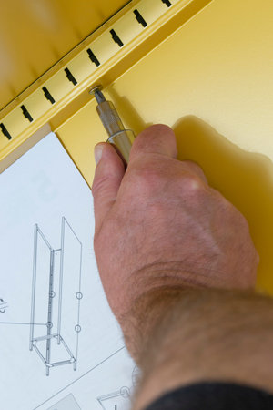 Man assembling a yellow metal cabinet with a screwdriver and instructions.  Self assembly flat pack...