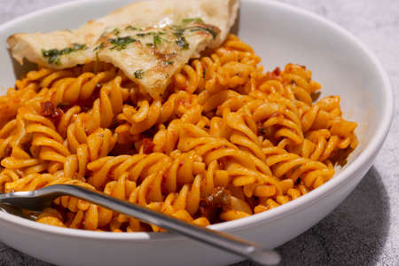Fusilli pasta in a tomato sauce with garlic bread in a bowl.  Concrete backgroundの写真素材