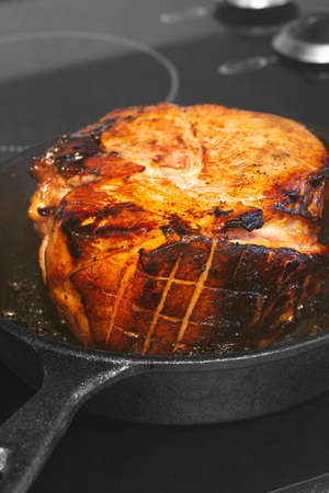 Searing a glazed gammon ham joint of meat.  In a cast iron frying pan on a hob stove.の写真素材