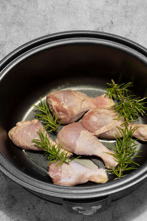 Raw chicken drumsticks with rosemary in a slow cooker ready for cooking.  Concrete backgroundの写真素材