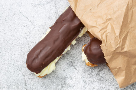 Chocolate eclair with a custard cream filling in a brown paper bag. Environmentally friendly...