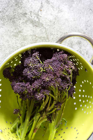 Purple sprouting broccoli washed in a green colander.  On a concrete backgroundの写真素材