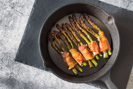 Asparagus wrapped in back bacon cooked in a cast iron frying pan.  On a slate cutting boardの写真素材