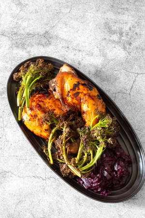Piri or Peri chicken dinner with roasted broccoli and pickled red cabbage on a black plate.  On a concrete backgroundの写真素材