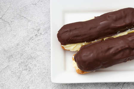 Chocolate eclair with a custard cream filling on a white plate.  With a concrete backgroundの写真素材