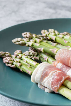 Asparagus wrapped in back bacon on a blue green plate.  With a concrete backgroundの写真素材