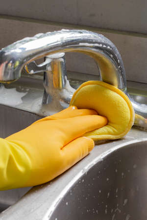 Person, wearing rubber gloves, cleaning a chrome tap in a kitchen, with a foam padの写真素材