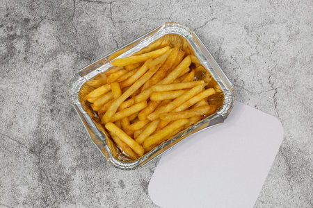 French fries in a foil takeaway tray with lid. On a concrete background