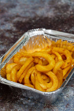 Curly fries in a takeaway foil tray.  On a grunge backgroundの写真素材