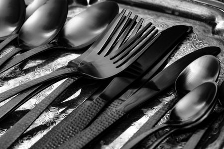 Set of black cutlery tableware on an antique silver tray.  On a wood background