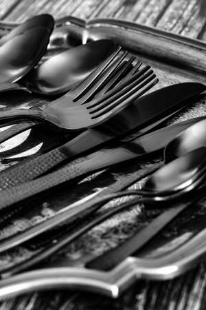 Set of black cutlery tableware on an antique silver tray.  On a wood backgroundの写真素材