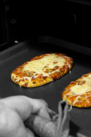 Vegetable pizza on a baking tray, being taken out of an oven.  With selective colourの写真素材