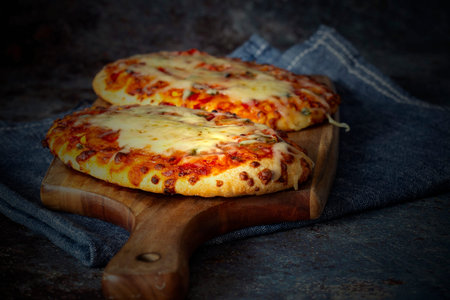 Vegetable pizza with melted cheese cooked on a wooden chopping board. With a tea towel on a grunge...