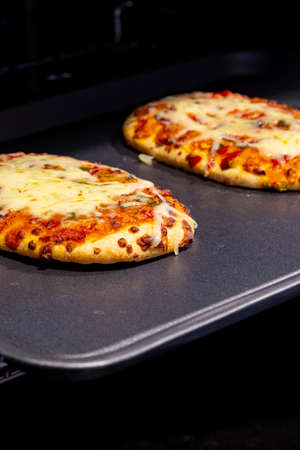 Vegetable pizza with melted cheese cooked on a baking tray in an oven.の写真素材