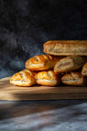 Sausage rolls, freshly baked and cooling on a wooden chopping board. On a Black stone backgroundの写真素材