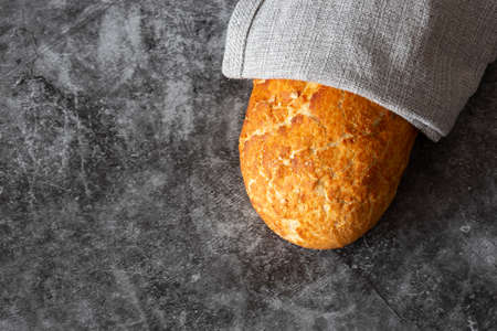 Tiger loaf of bread wrapped in a grey tea towel. On a black stone backgroundの写真素材
