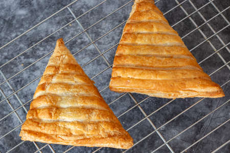 Apple turnover, freshly cooked, cooling down on a metal cooling rack. On a dark stone backgroundの写真素材