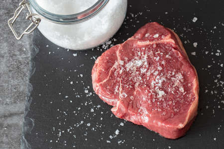 Rump beef steak, seasoned with sea salt with jar in background, on a slate chopping board. On a dark stone backgroundの写真素材