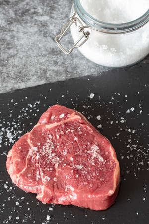 Rump beef steak, seasoned with sea salt with jar in background, on a slate chopping board. On a dark stone backgroundの写真素材