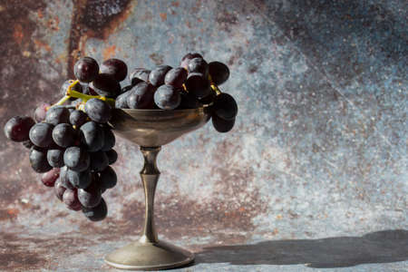 Bunch of black grapes in an old pewter goblet. On a grunge backgroundの写真素材