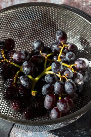 Bunch of black grapes in a metal colander strainer. On a grunge background