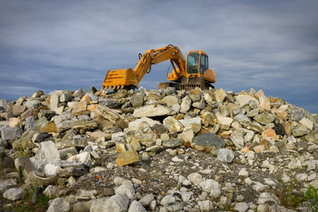 yellow excavator on top of big heap of stones