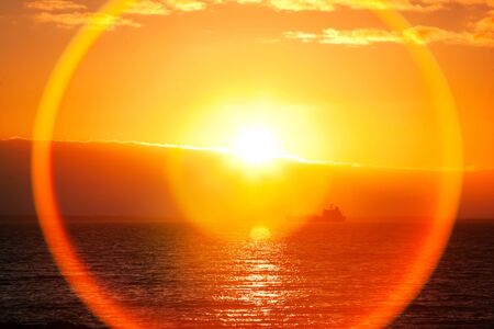 Beautiful Sunrise over ocean bay and silhouette of ship, lens flare effectの写真素材