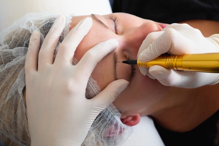 Cosmetologist making permanent makeup on woman's faceの写真素材