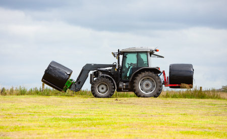 tractor collecting a roll haystack in the field at nice blue sunny dayの写真素材