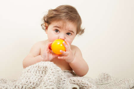 Baby boy playing with yellow ball on knitted blanketの写真素材