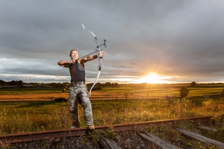 Tough man with bow and arrows during dramatic cloudy sunset.の写真素材