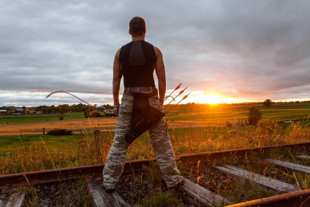 Tough man with bow and arrows during dramatic cloudy sunset.の写真素材