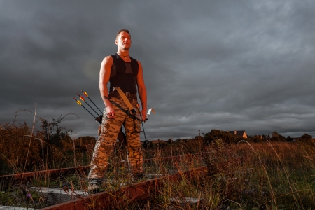 Tough man with bow and arrows during dramatic cloudy sunset.の写真素材