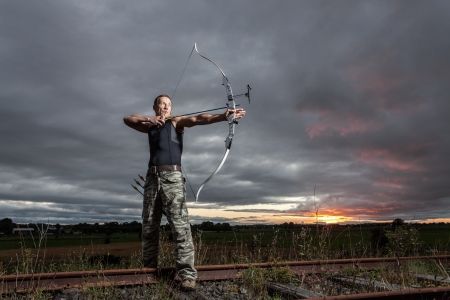 Tough man with bow and arrows during dramatic cloudy sunset.の写真素材