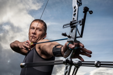 Tough man with bow and arrows, close up with cloudy sky at backgroundの写真素材