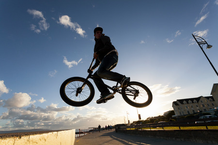 Young man performs BMX stunts during sunset at the street の写真素材