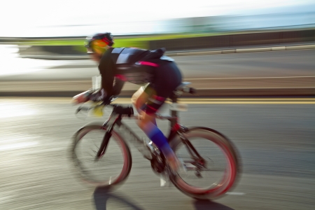 Athlete riding bicycle at sunny day on coastal road, blurred motion