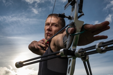 Tough man with bow and arrows, close up with cloudy sky at background.の写真素材
