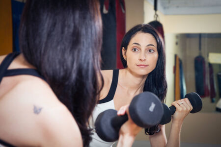 Nice fitness brunette woman working out with dumbbells in gymの写真素材