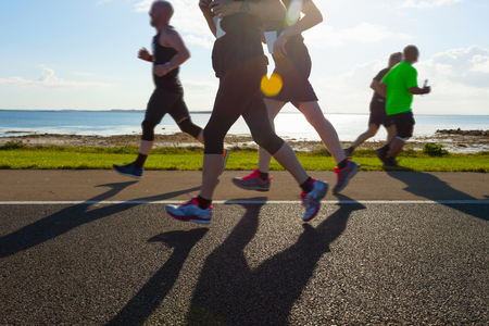 Group of runners compete in the race on coastal roadの写真素材
