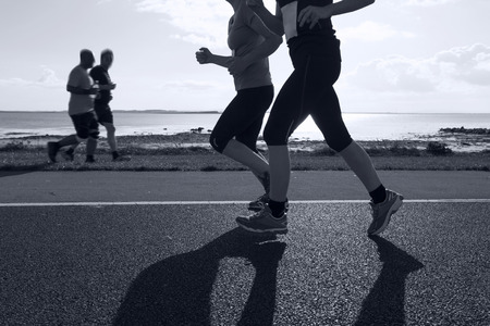 Group of runners compete in the race on coastal roadの写真素材