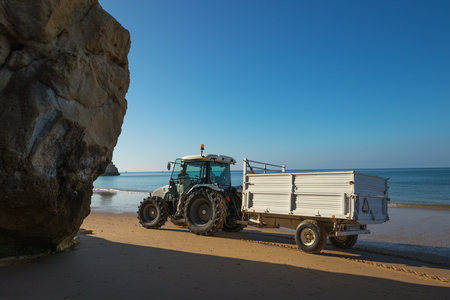 Tractor with trailer carry out beach maintenance on the ocean coast in Portugal.の写真素材