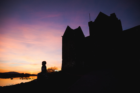 Boy looking at colorful sunset at the ocean bay with Castle siluette.の写真素材