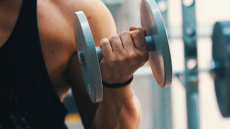 Sports bodybuilder young man hard training biceps muscles in gymの写真素材