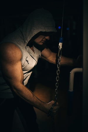A strong bodybuilder makes triceps exercises with a chain in the gym.の写真素材