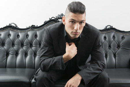 Young man in business suit sitting on leather sofaの写真素材