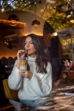 Young woman sitting in cafe drinking coffee seen through display windowの写真素材