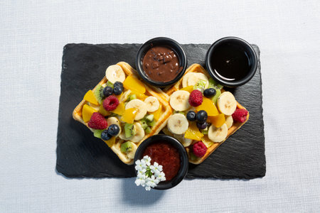 Waffle served on black stone  with fresh fruits and chocolateの写真素材