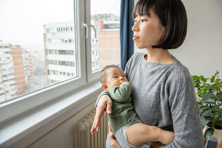 Mother holding her newborn son, looking through window