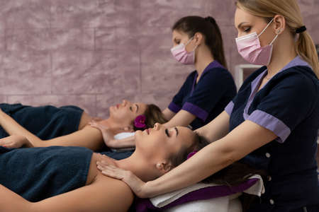 Two women doing relaxing  massage in spa center wearing protective coronavirus masksの写真素材